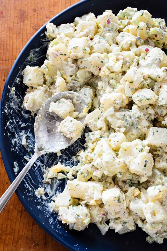 A blue bowl full of creamy potato salad with hardboiled eggs and a large spoon.
