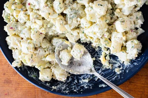 A blue bowl full of creamy potato salad with hardboiled eggs and a large spoon.