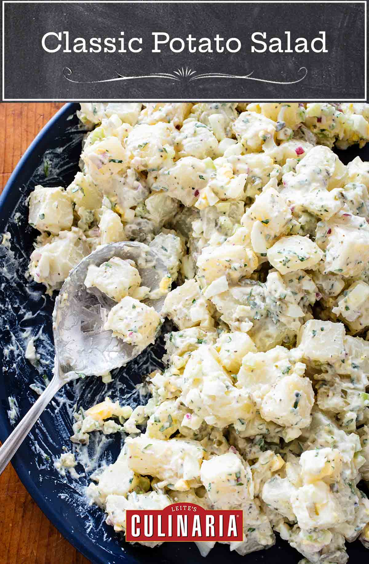 A blue bowl full of creamy potato salad with hardboiled eggs and a large spoon.