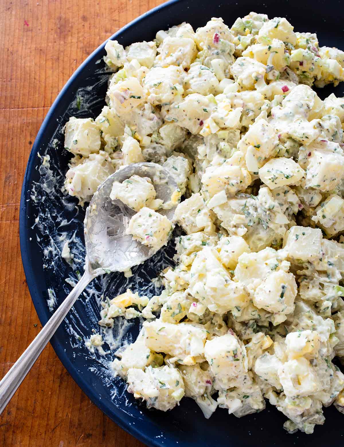 A blue bowl full of creamy potato salad with hardboiled eggs and a large spoon.