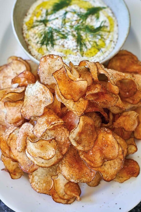 A white oval platter holding a bowl of dill dip with potato chips beside it.