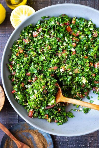A bowl of tabbouleh with a wooden spoon resting inside.