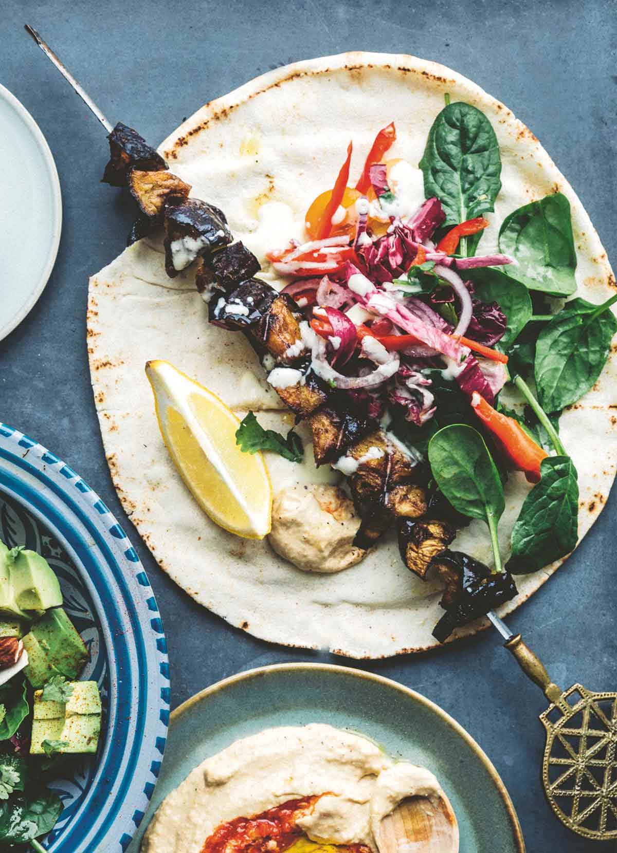 An eggplant kebab on a tortilla with fresh spinach, garlic sauce, and cabbage.