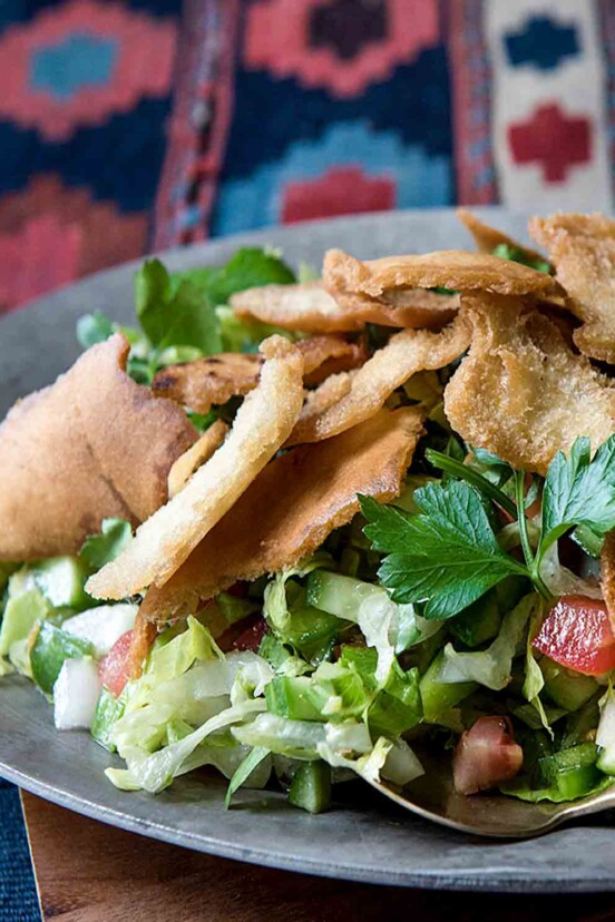 A plate of fattoush topped with crispy pita chips and a fork on the side.