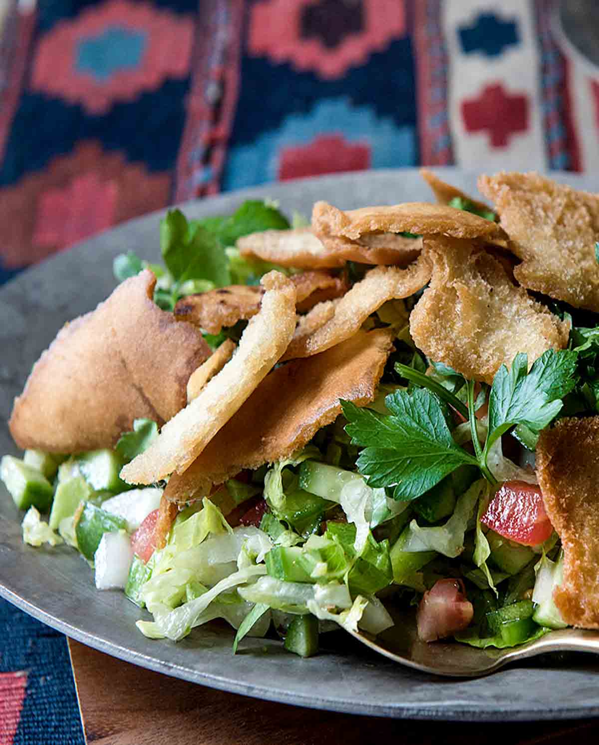 A plate of fattoush topped with crispy pita chips and a fork on the side.