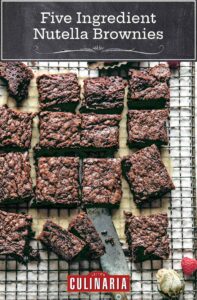A batch of five ingredient Nutella brownies cut into squares on a wire rack with fresh raspberries scattered around.