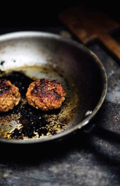 Two patties of Goan-style chourico being cooking in a metal skillet.