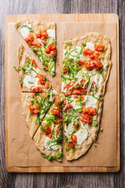 A grilled pizza with summer tomato sauce and scallions, cut into 8 wedges on a wooden board.