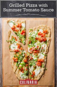 A grilled pizza with summer tomato sauce and scallions, cut into 8 wedges on a wooden board.