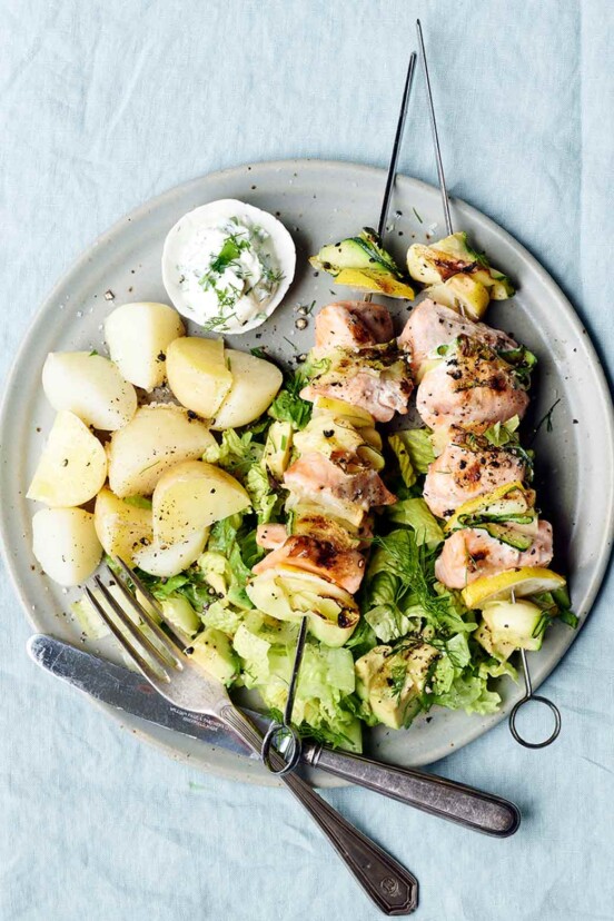 A plate with two grilled salmon and zucchini skewers with potatoes on the side
