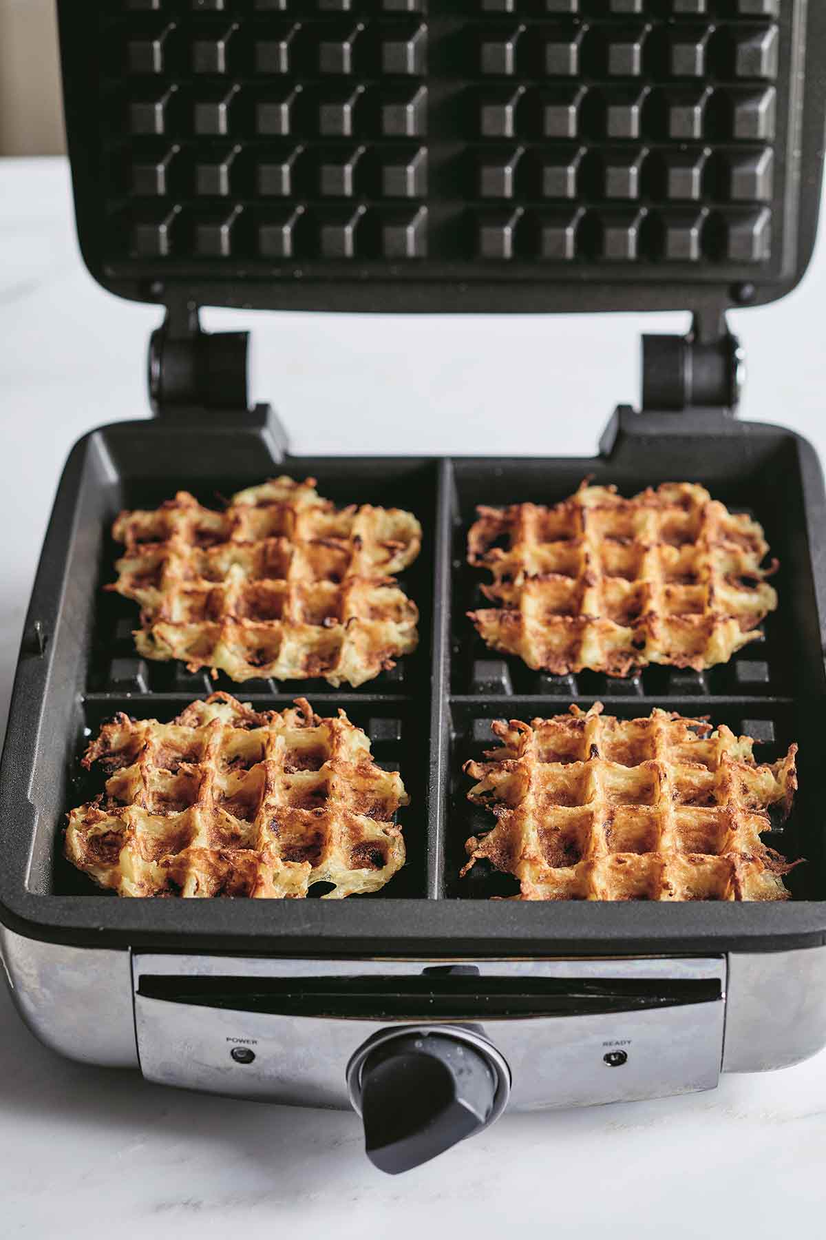 Four of Ina Garten's waffle iron hash browns in a waffle iron with the lid open.