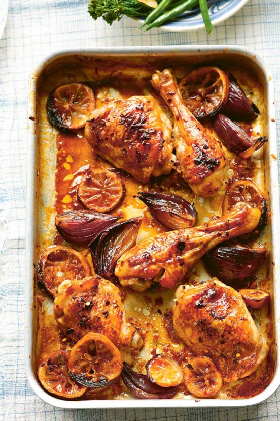 A metal sheet pan filled with lemon ginger chicken legs and thighs with shallots and lemon slices.