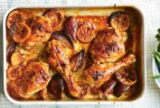 A metal sheet pan filled with lemon ginger chicken legs and thighs with shallots and lemon slices.