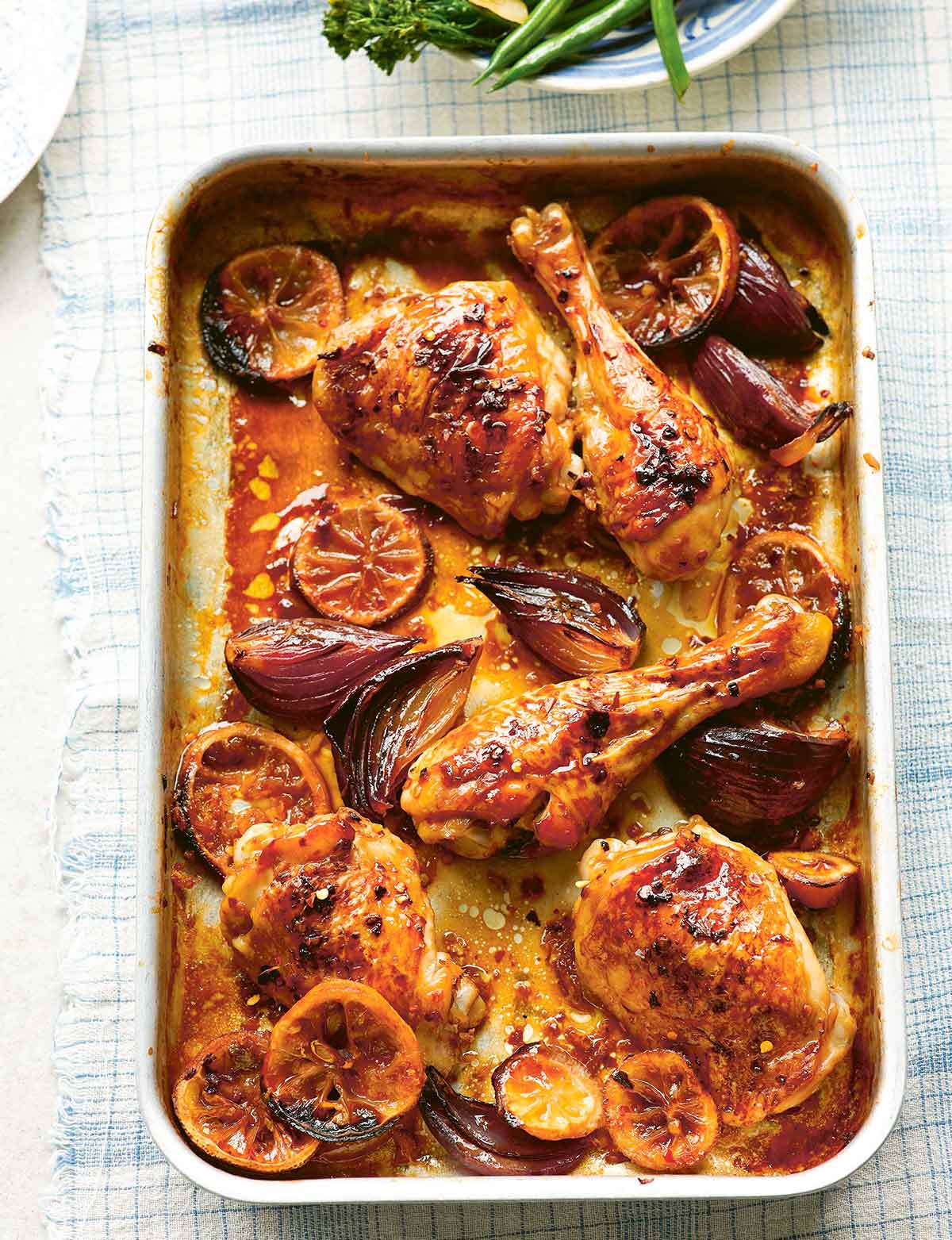 A metal sheet pan filled with lemon ginger chicken legs and thighs with shallots and lemon slices.