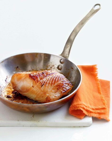 A piece of miso cod in a skillet with an orange napkin next to it.
