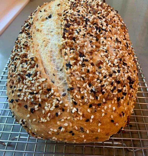 A loaf of no-knead everything bagel bread on a cooling rack.