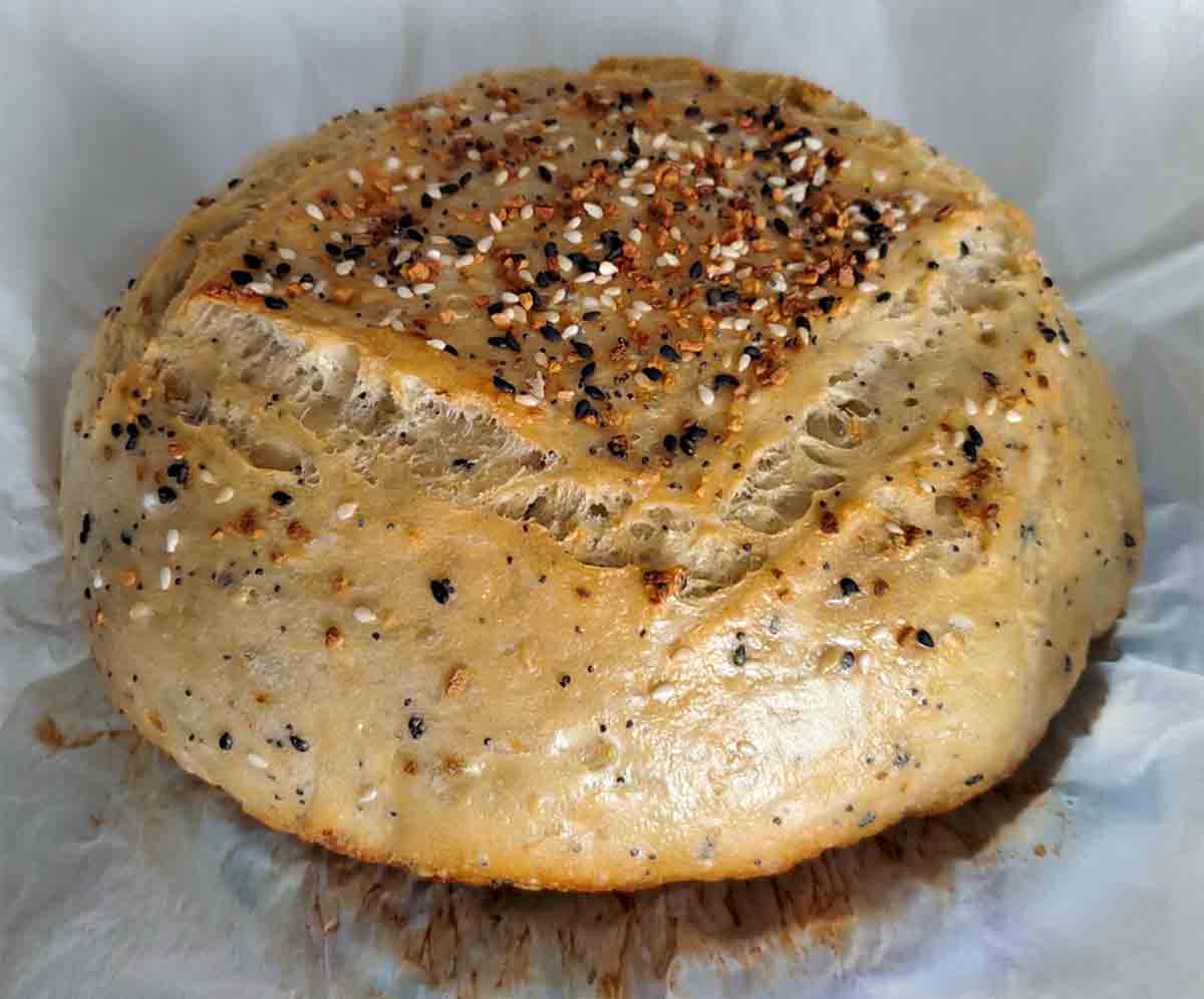 A loaf of no-knead everything bread on parchment.