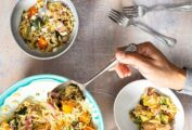 Several bowls of orzo salad with grilled vegetables and a person scooping some from a larger bowl.