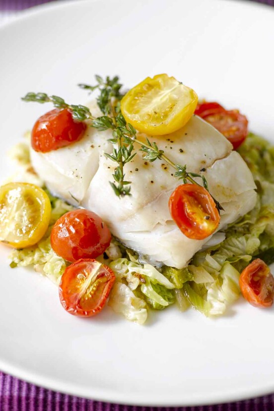 A piece of oven-roasted halibut with cherry tomatoes and thyme on a bed of cooked cabbage.