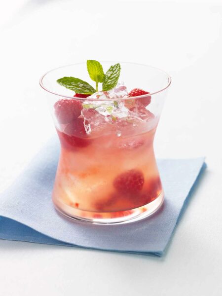A glass of raspberry lemonade with tequila garnished with a mint sprig.