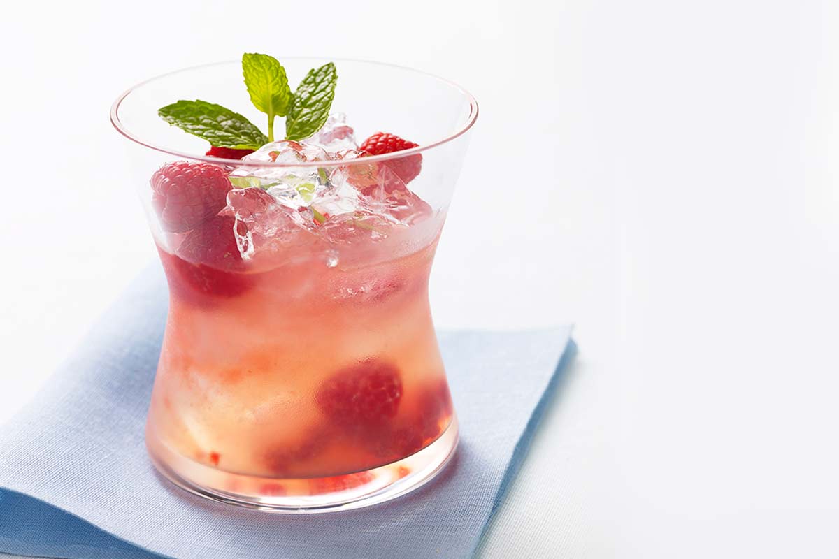 A glass of raspberry lemonade with tequila garnished with a mint sprig.
