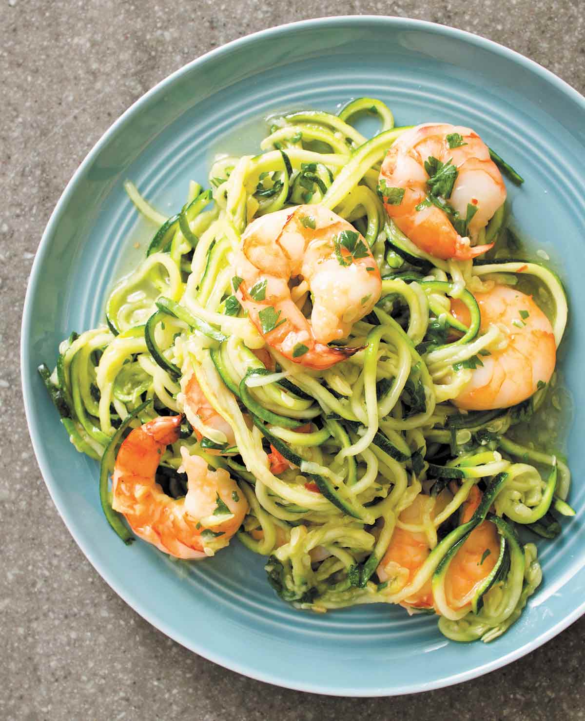 A blue plate topped with shrimp scampi with zucchini noodles.