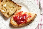 Two pieces of buttered toast, one with strawberry jam, on a white plate.