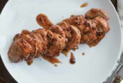 A sliced smoked pork tenderloin with maple chipotle glaze on a white plate.