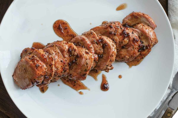 A sliced smoked pork tenderloin with maple chipotle glaze on a white plate.