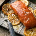 A piece of smoked salmon with bourbon marinade on a baking sheet with lemon slices and a fork.