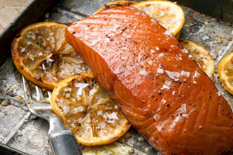 A piece of smoked salmon with bourbon marinade on a baking sheet with lemon slices and a fork.