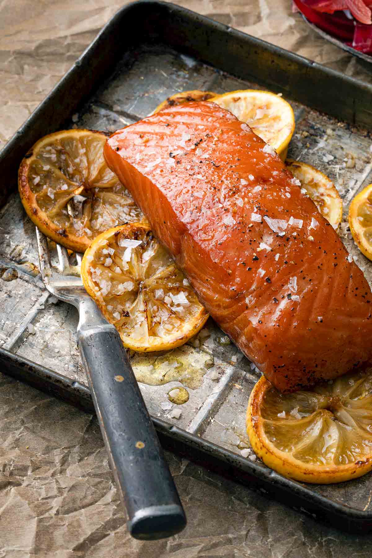 A piece of smoked salmon with bourbon marinade on a baking sheet with lemon slices and a fork.