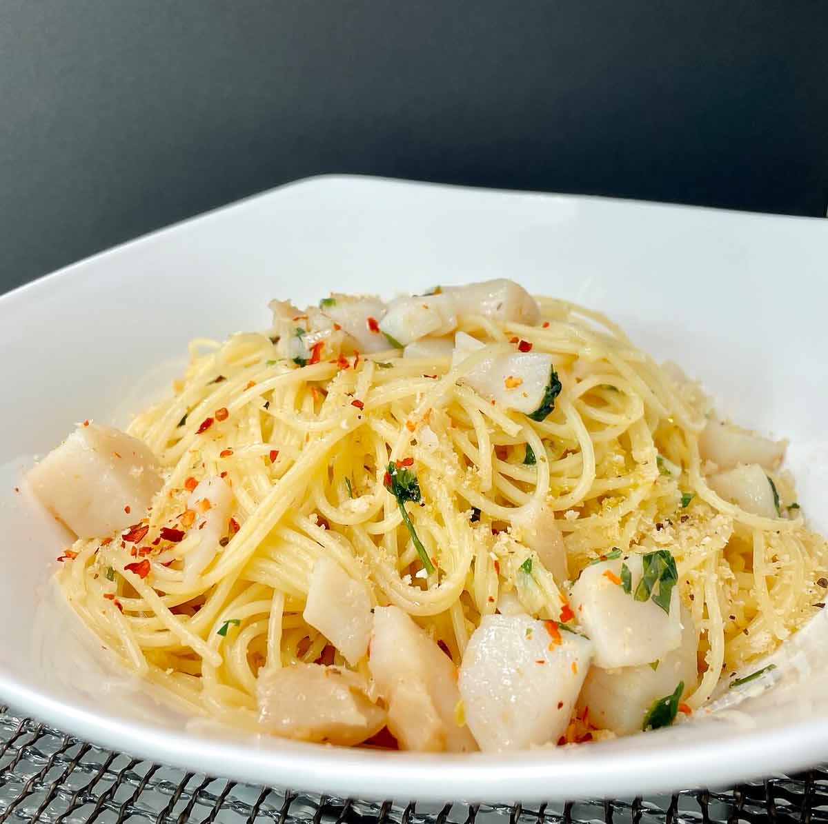 A bowl of spaghetti with scallops, topped with pepper flakes and parsley.