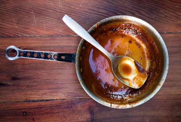 A small pot with a small amount of spicy bourbon barbecue sauce left in it and a spoon resting inside.