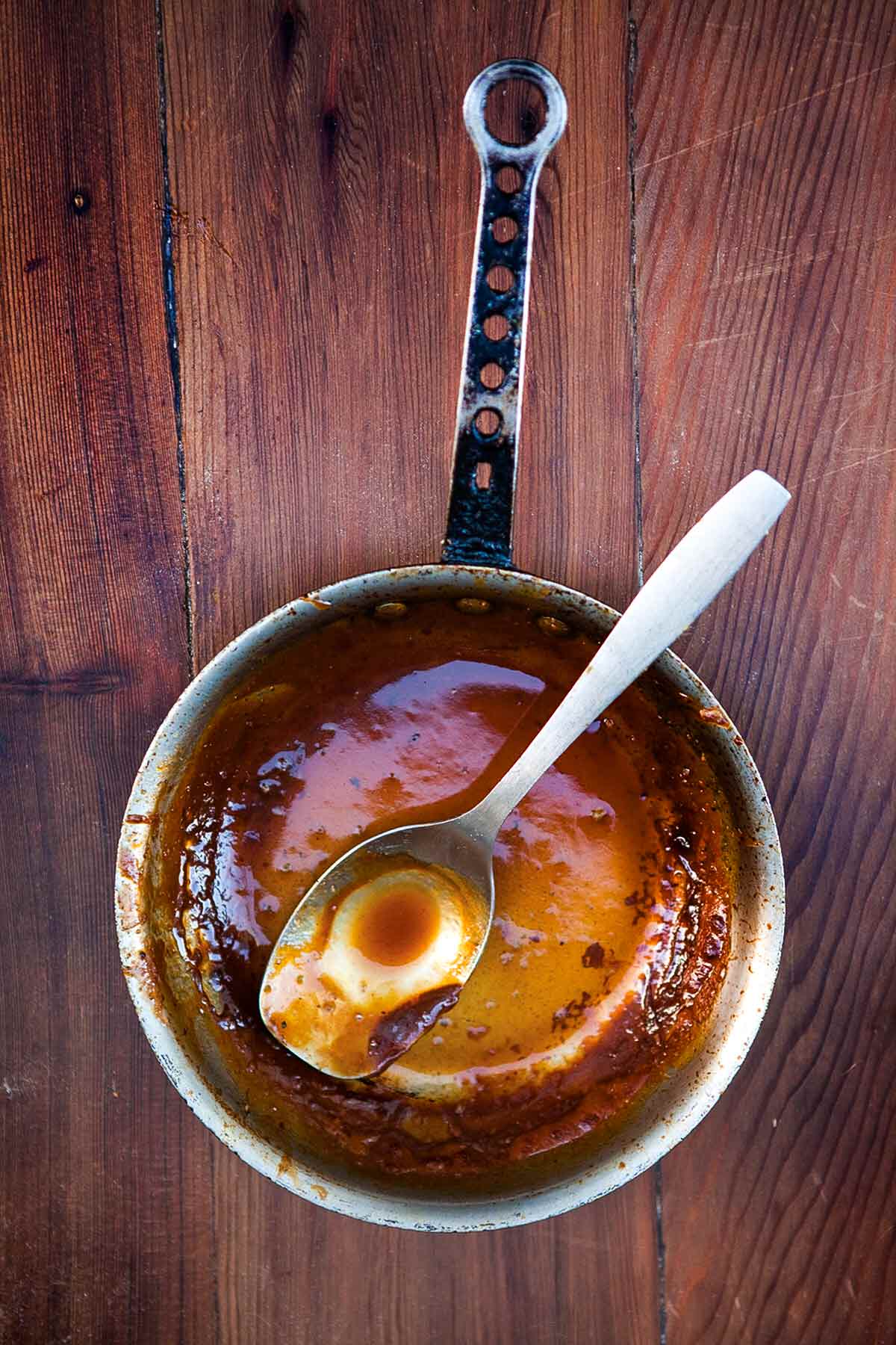 A small pot with a small amount of spicy bourbon barbecue sauce left in it and a spoon resting inside.