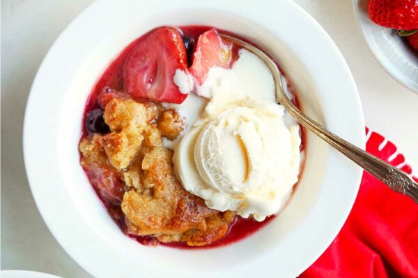 Two white bowls filled with strawberry blueberry cobbler and topped with ice cream.