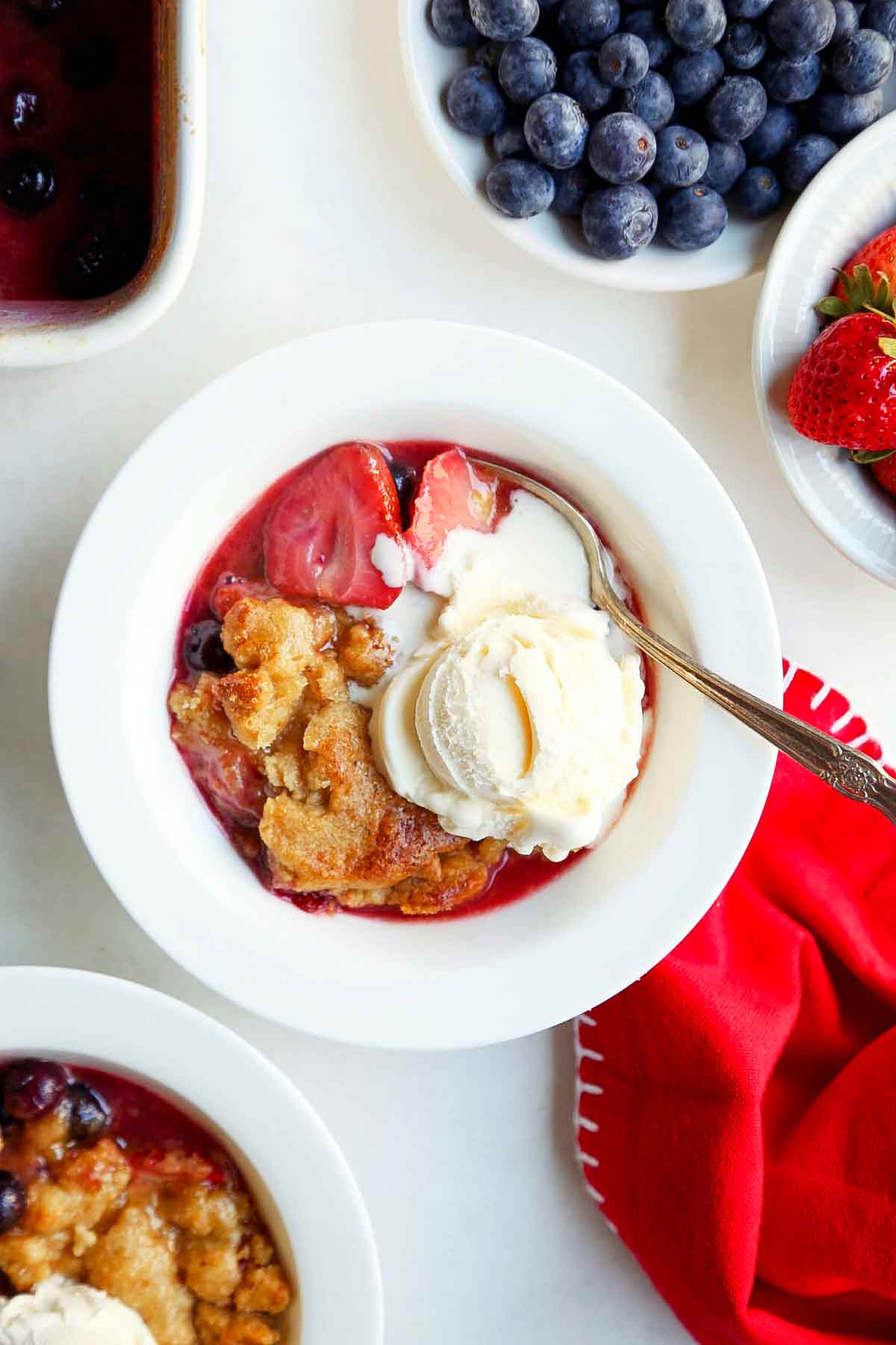 Two white bowls filled with strawberry blueberry cobbler and topped with ice cream.