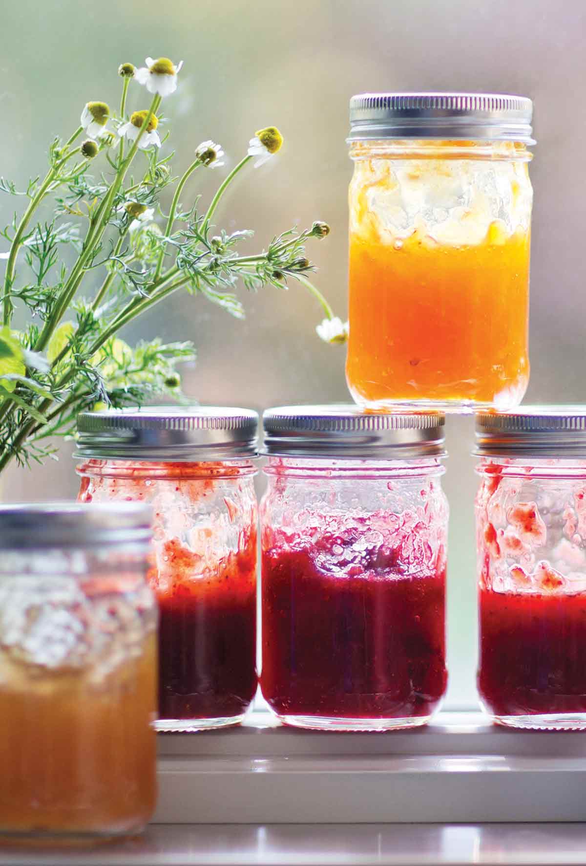 Five jars of jam, two apricot and three strawberry rhubarb jam, with some wildflowers.