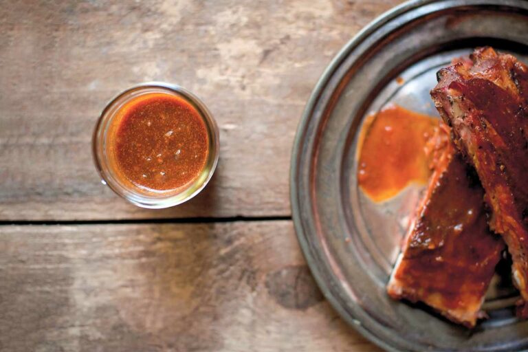 A platter of ribs covered with Texas-style barbecue sauce, and a glass of extra sauce on the side.