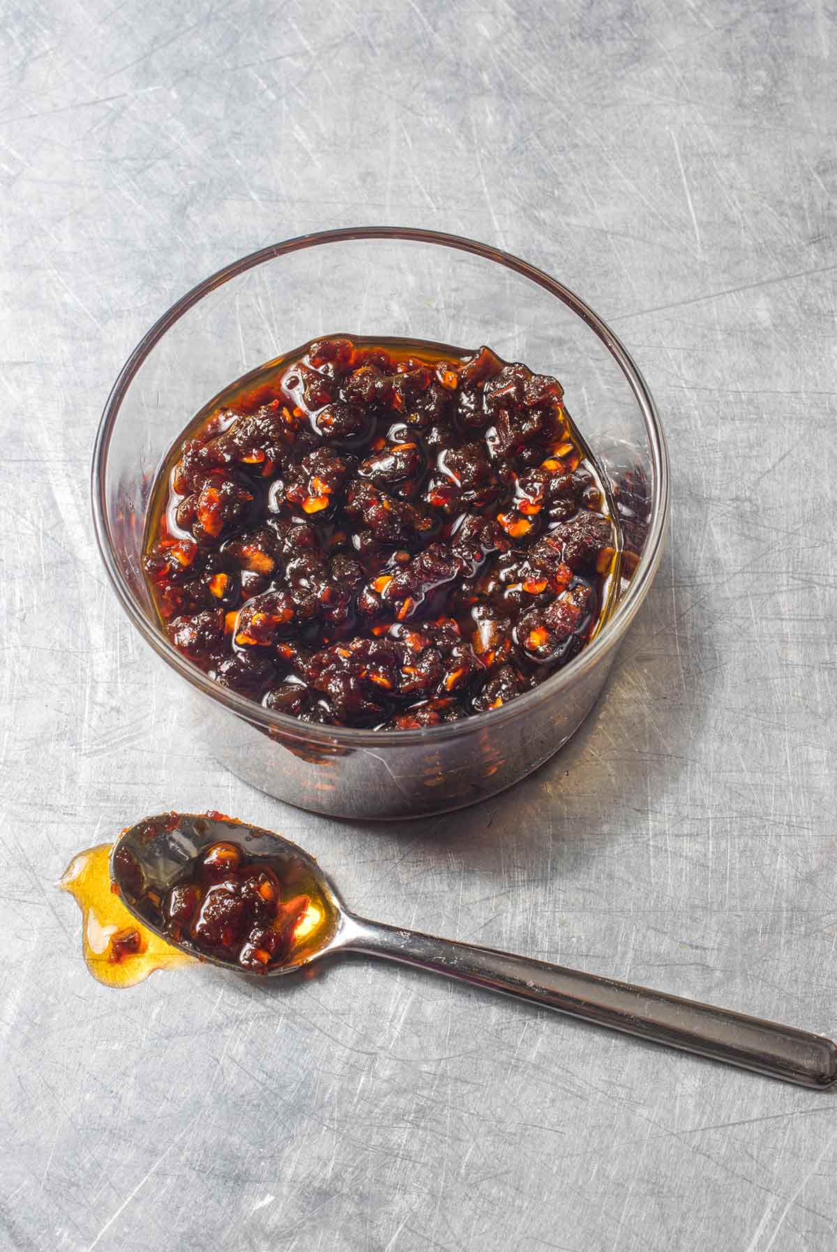 A glass bowl partially filled with Thai chili jam and a spoon on the side.