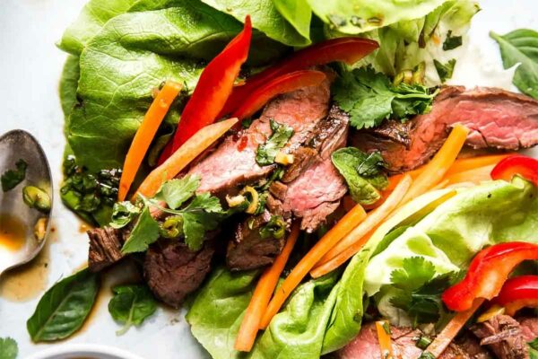 Three assembled Thai-style sliced beef lettuce wraps with a bowl of dipping sauce on the side.