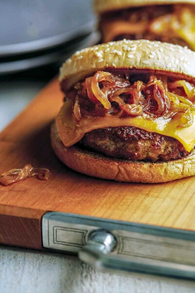 A turkey burger with maple caramelized onions and cheese on a wooden cutting board.