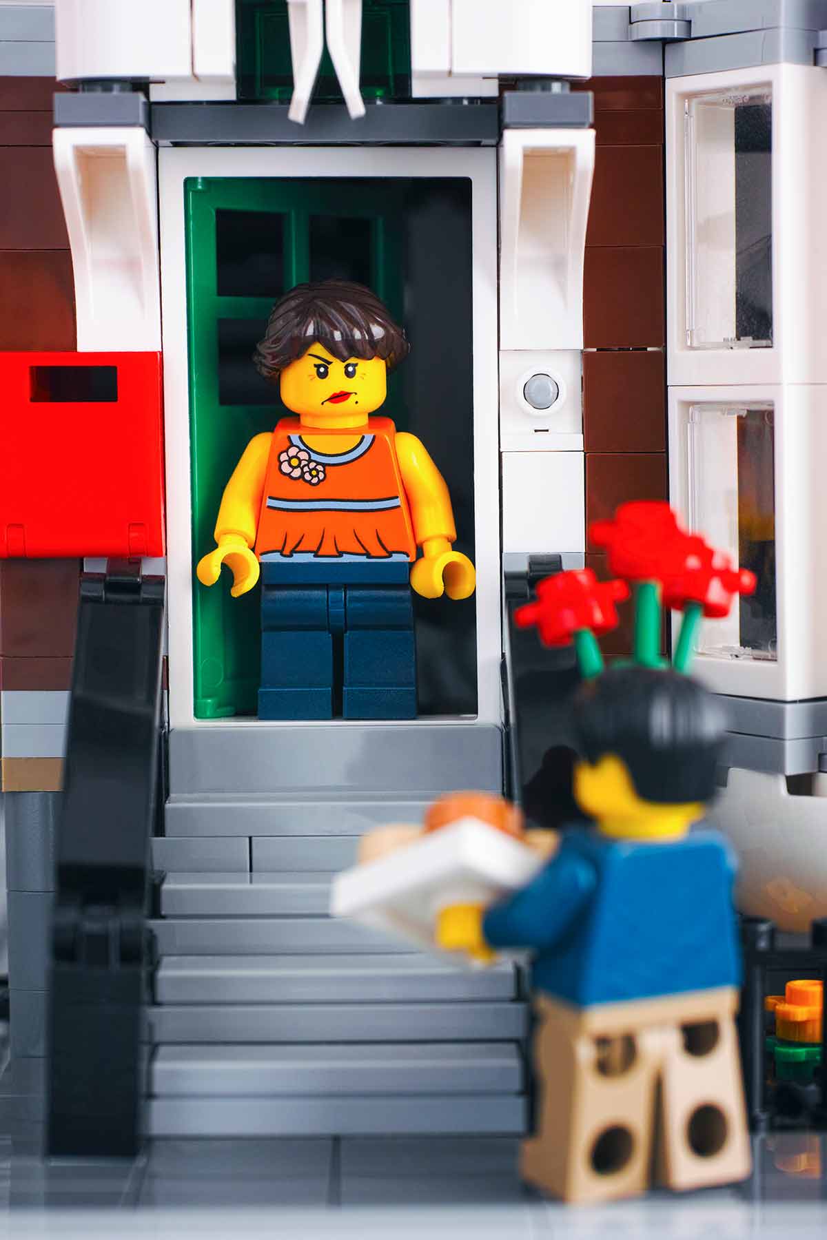 A Lego scene of an unexpected weekend guys arrinving with flowers; a Lego host looks angry