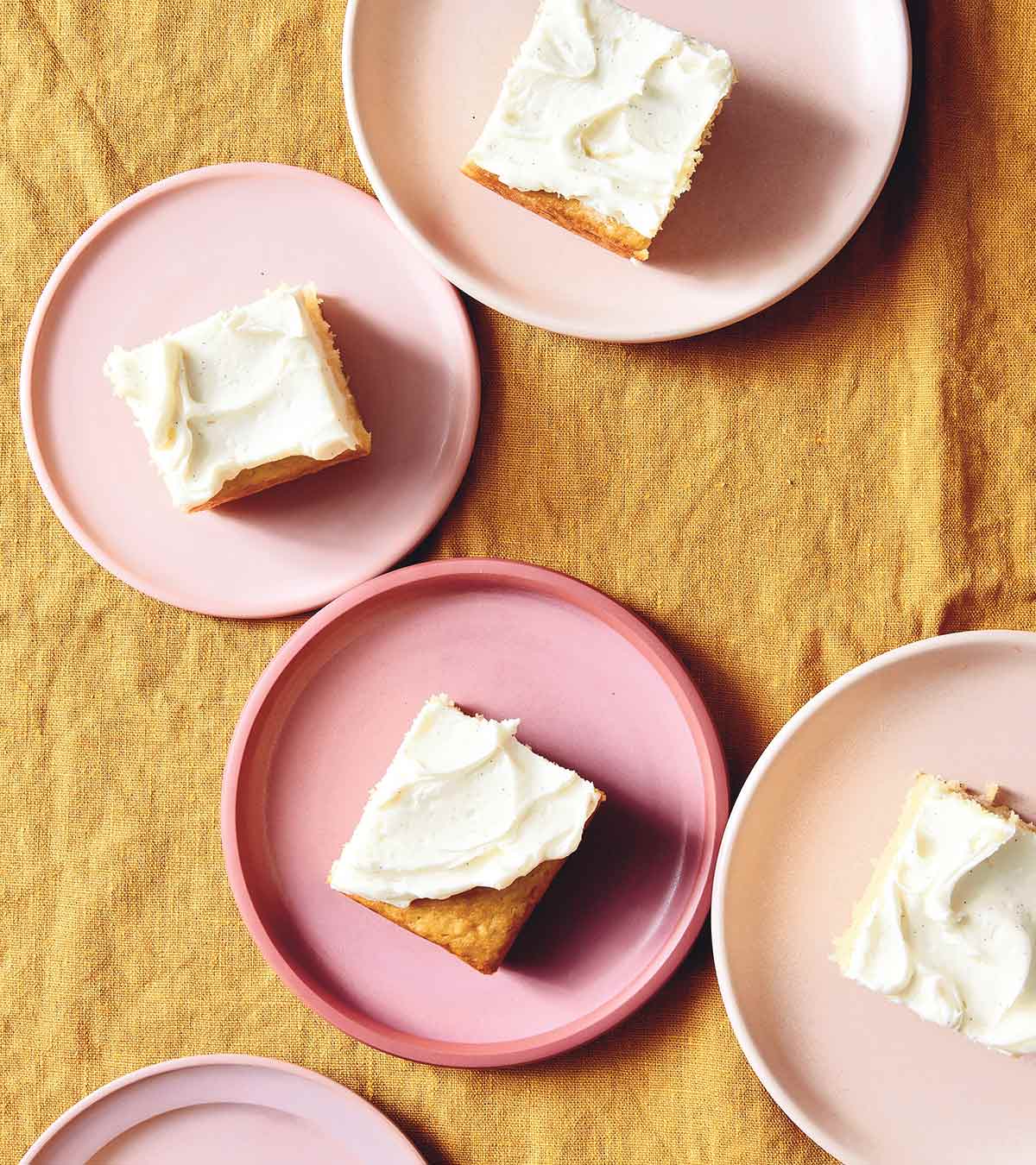 Individual servings of vanilla buttermilk cake with white frosting on pink plates.