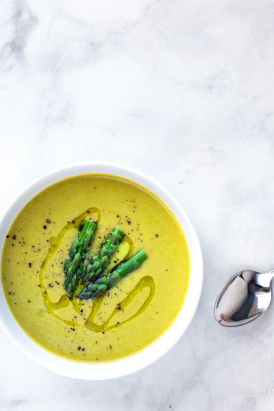 A white bowl filled with vegan asparagus soup with white beans with asparagus tips, ground pepper, and a drizzle of oil on top.