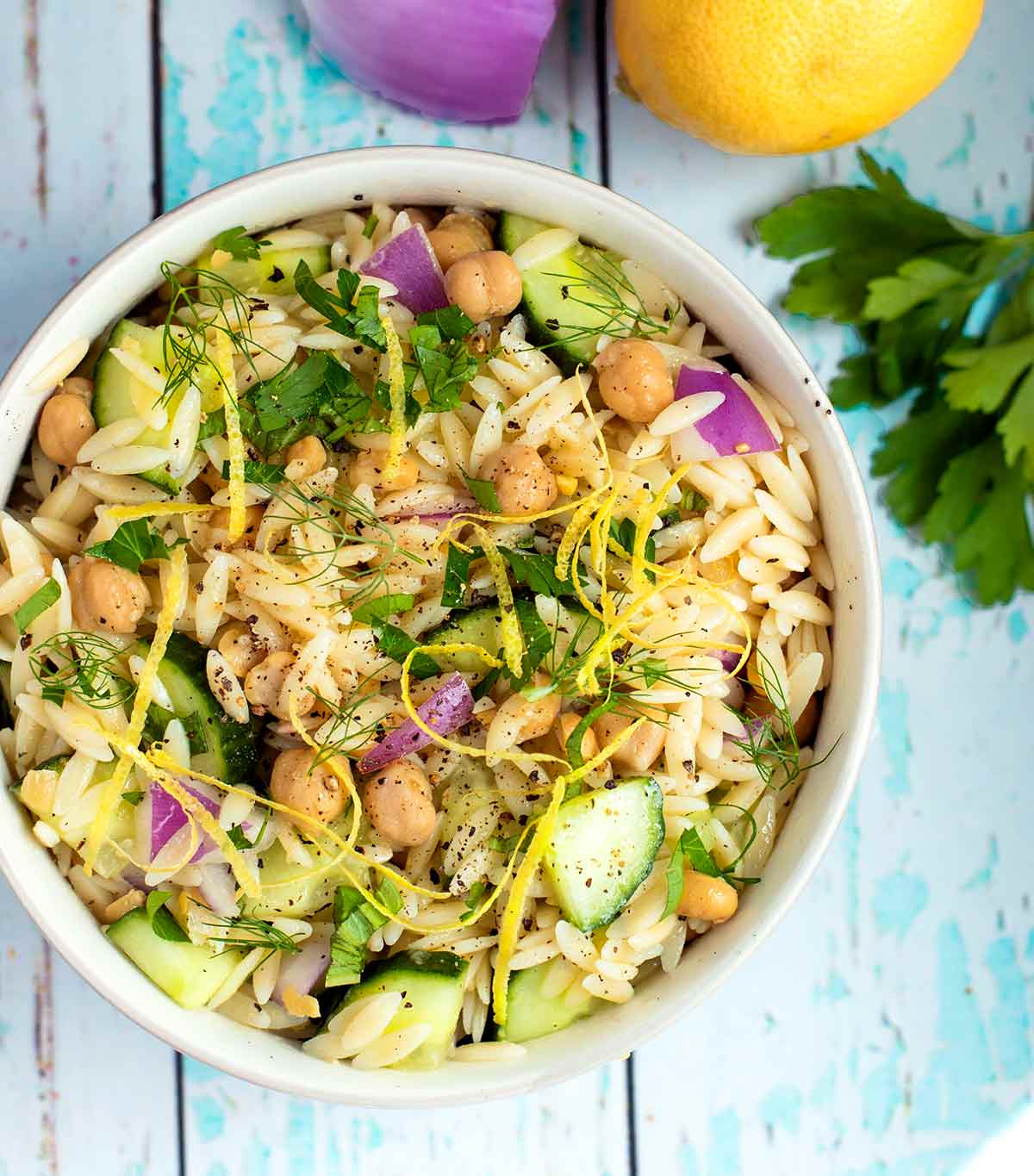 A white bowl filled with vegan chickpea and orzo salad with lemon zest garnish.