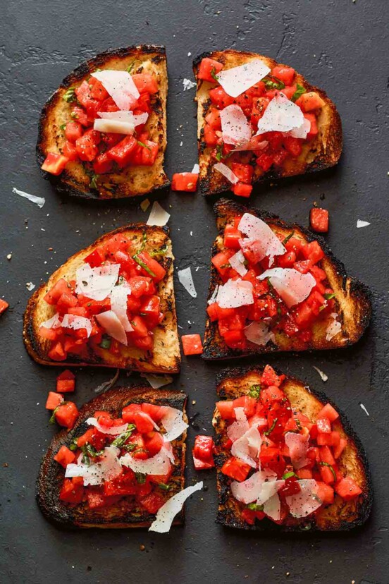 Three watermelon and tomato bruschetta slices topped with shaved pecorino and cut in half.