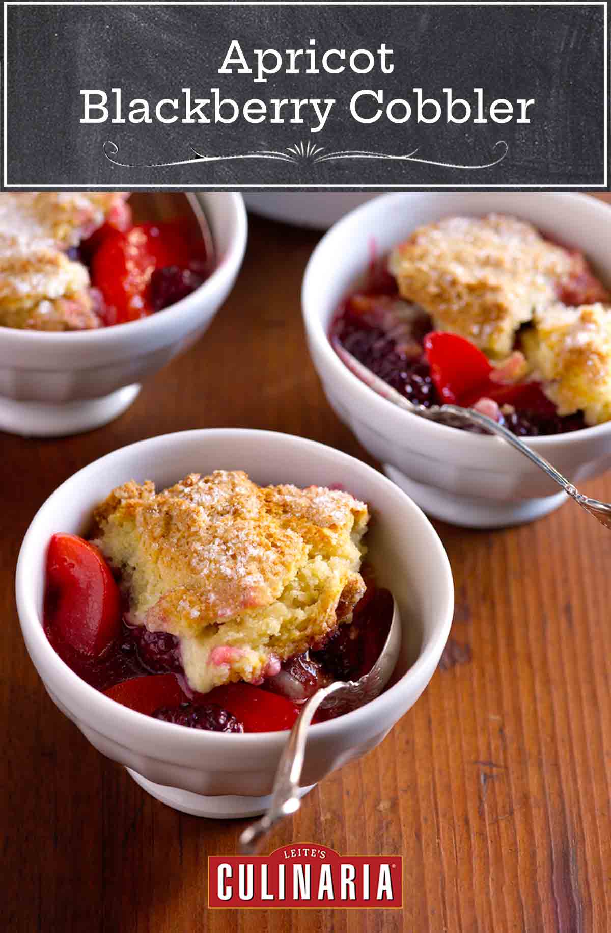 Small white bowls with spoons, filled with apricot and blackberry compote, coered with dollops of sugared biscuit topping.