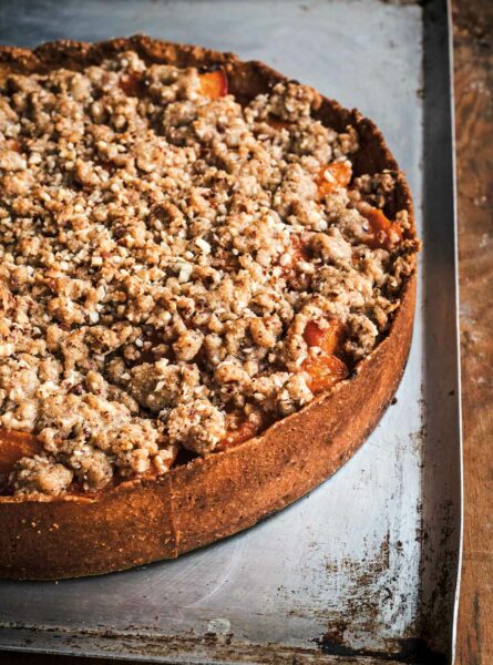 An apricot tart with high sides and a crumble topping, sitting on a metal cookie sheet.