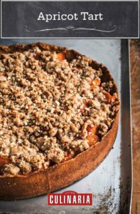 An apricot tart with high sides and a crumble topping, sitting on a metal cookie sheet.